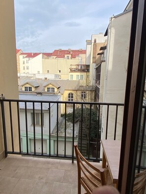 Un balcón con vistas a edificios cercanos, una silla y una barandilla.