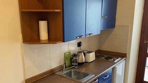 Una cucina compatta con mobili blu, un lavello in acciaio inossidabile e un piccolo frigorifero.