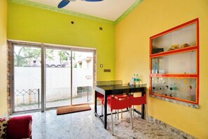 A room with a glass table, red chairs, a yellow wall, and a sliding glass door leading outside. - iROOMZ Tilottama Guest House (Basirhat)