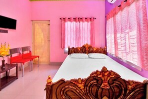 A bedroom with a large bed, a desk, two chairs, and a TV on the wall. - iROOMZ Tilottama Guest House (Basirhat)