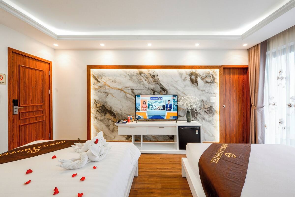Habitación de hotel con una cama grande, un escritorio con televisor de pantalla plana, un refrigerador pequeño y una pared de mármol.