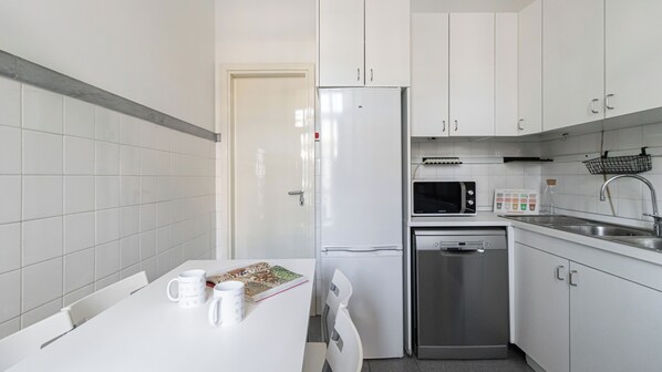 A compact kitchen with white cabinets, a refrigerator, a microwave, a dishwasher, and a sink.