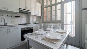 A modern kitchen with white cabinets, a stove, and a dining area set for four with wine glasses and plates.