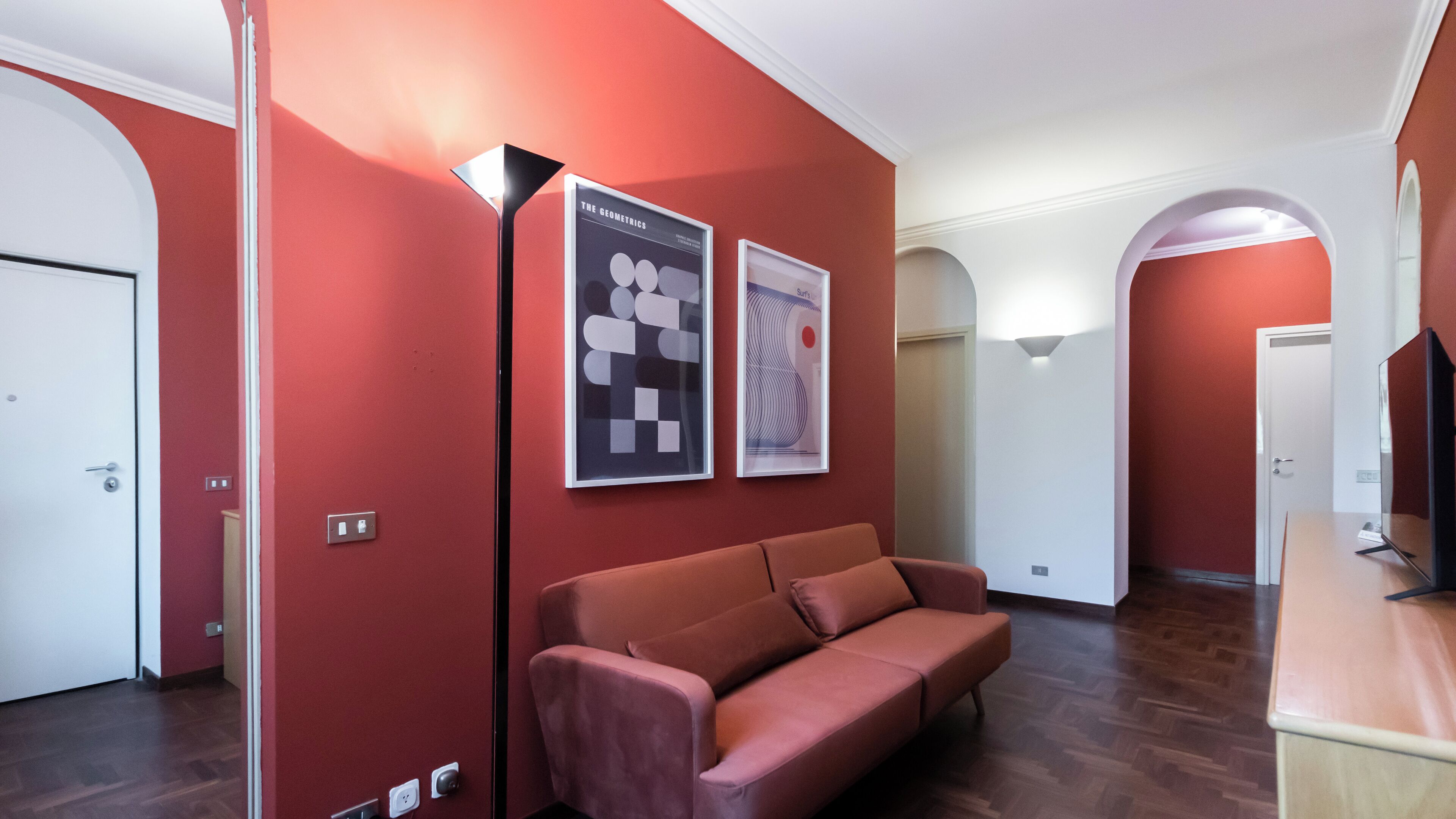 A modern interior with red walls, a leather sofa, and two framed posters.