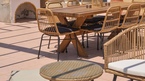 En udendørs terrasse med et træbord og fletstole, et lille rundt bord og en stenovn.