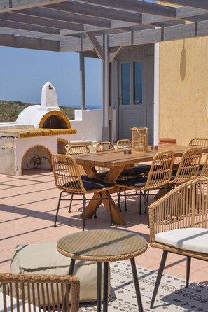 Un patio al aire libre con una mesa de madera y sillas de mimbre, una mesita redonda y un horno de piedra.