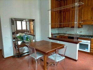 Una cucina con mobili in legno, un lavandino in acciaio inossidabile e un'area pranzo con tavolo in legno e sedie trasparenti.