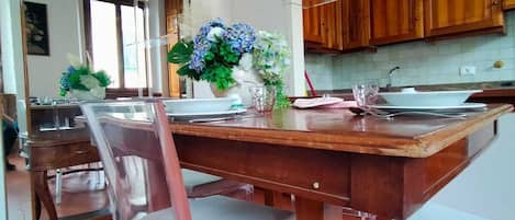 A dining area with a wooden table and chairs, a vase of flowers, and wooden cabinets in the background.