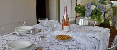 A dining table set with white plates, cutlery, a glass, a bottle of rose wine, and a bowl of snacks.