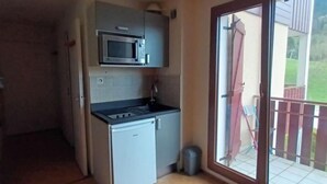Una cocina compacta con microondas, lavamanos y refrigerador pequeño.