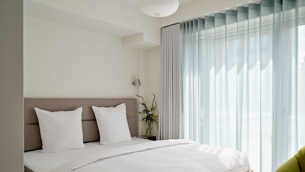 A modern bedroom with a wooden bed frame, white bedding, and a large window with sheer curtains. - Studio Apartment for 2 with Terrace (København)