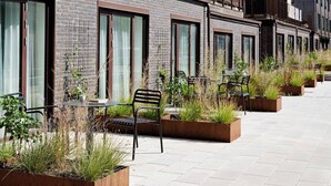 Une rangée d’espaces de détente en plein air, avec des chaises et des tables en métal, entourée de jardinières contenant différentes plantes.
