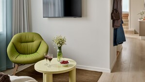Una sala de estar moderna con un televisor de pantalla plana, un sillón verde, una mesa redonda con un florero y copas de vino, y un sofá marrón.