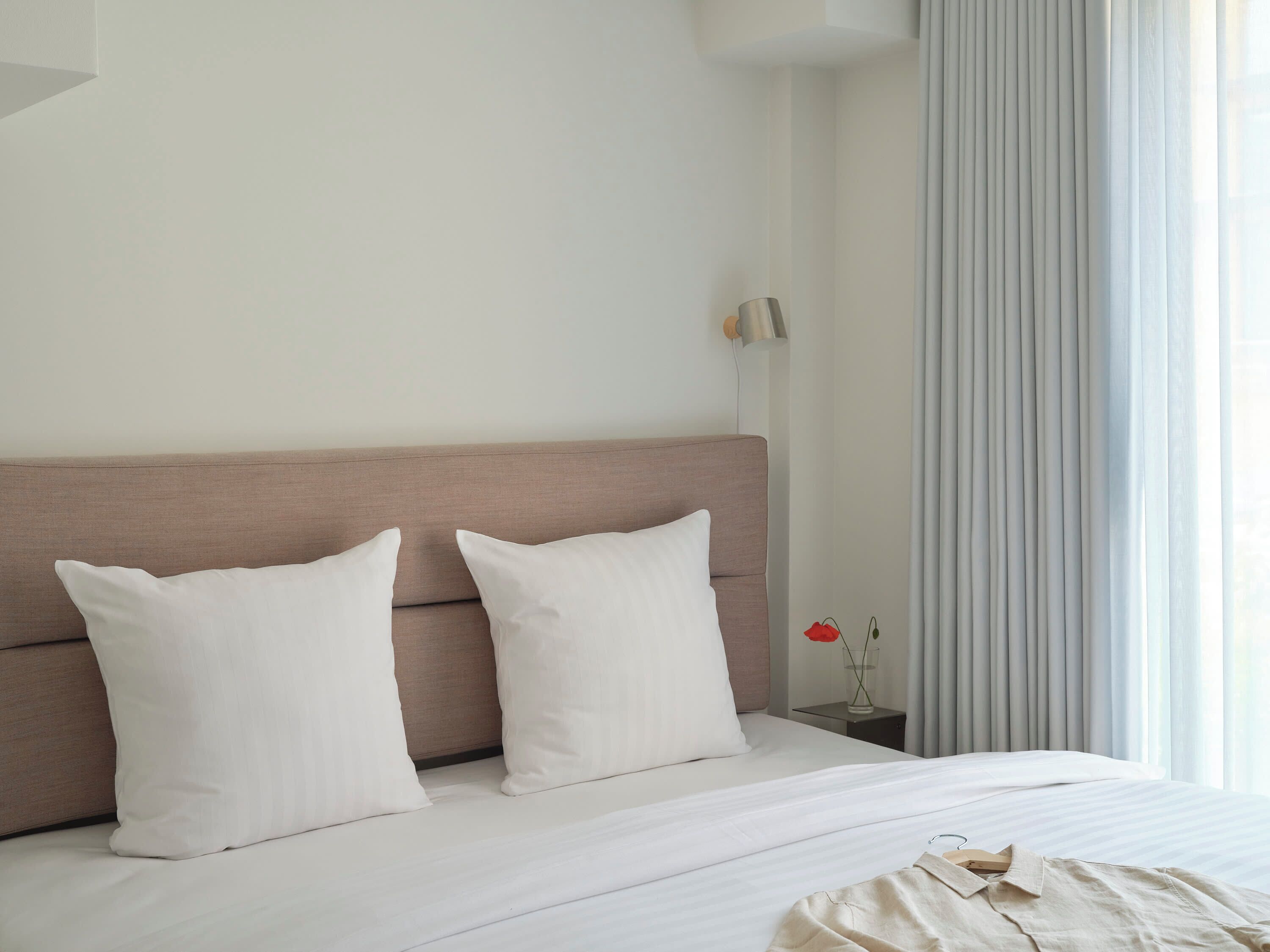 Una cama bien hecha con un cabecero de color claro y dos almohadas blancas.