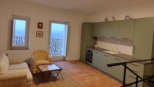 A compact living space with a kitchenette, a sofa, a chair, and a view through a window. - Casa in Collina - nel Borgo di Tenaglie (montecchio)
