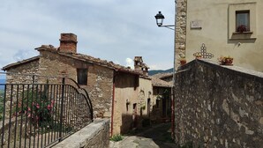 A narrow cobblestone street flanked by rustic stone buildings with traditional architecture, a wrought iron gate, and a clear sky above. - Casa in Collina - nel Borgo di Tenaglie (montecchio)
