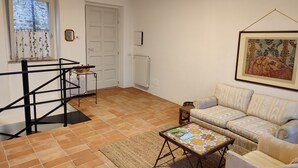A living room with a sofa, a coffee table, a staircase, and a door. - Casa in Collina - nel Borgo di Tenaglie (montecchio)