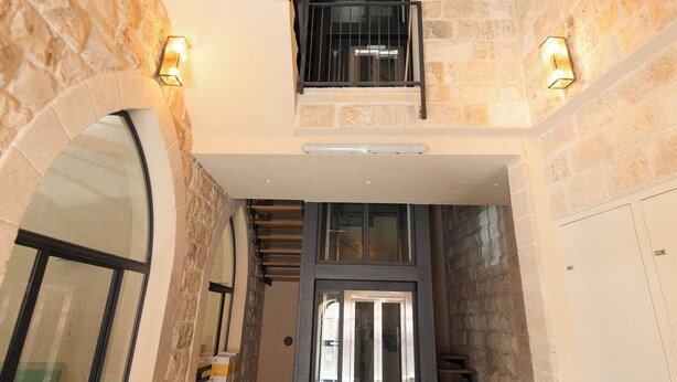 A spacious interior with a staircase leading to a mezzanine, stone walls, and a modern elevator. - PORT CITY HAIFA -  Flea Market Luxury (Haifa)