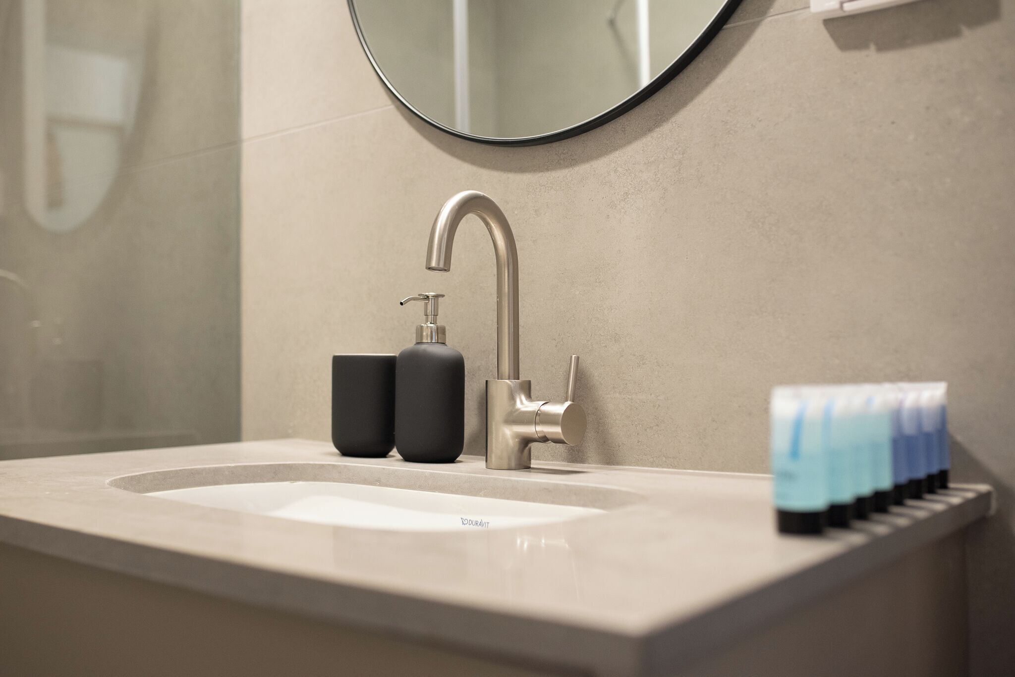 Un lavabo de salle de bain doté d’un robinet moderne, de deux distributeurs de savon noirs et d’une rangée de flacons bleus et blancs sur le comptoir.