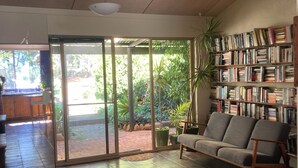 Ein geräumiger Wohnbereich mit einem großen Schiebeglastür, die zu einem Garten führt, einem Bücherregal voller Bücher und einem bequemen Sofa.