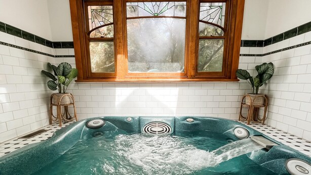 Een spa-ruimte met een groot bad, een raam met glas-in-lood en potplanten.