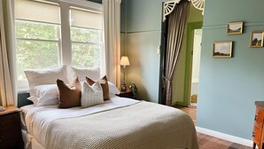 Een net opgemaakt bed met een wit-beige deken, een bedlampje en een nachtkastje met een klok.