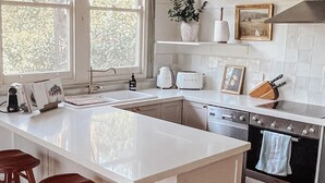 Een moderne keuken met een groot eiland, houten krukken, een spoelbak, een fornuis en een raam met jaloezieën.