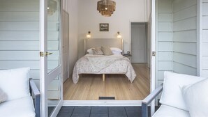 A bedroom with a bed, two bedside lamps, a hanging light fixture, and a door leading to another room. - Woolrich House - Woolrich House at Woolrich Estate (Olinda)