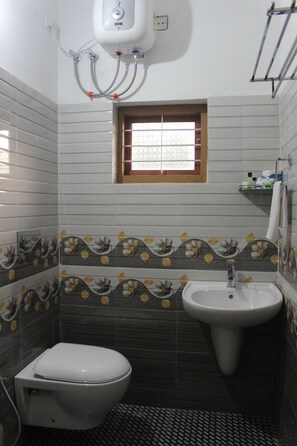 A bathroom with a toilet, sink, and a window. - Deluxe Room with Balcony (Vythiri)