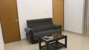 Una habitación con un sofá gris, una mesa de centro de vidrio y una puerta de madera.