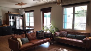 Una sala de estar con un sofá de cuero marrón, una mesa de comedor y una zona de cocina con electrodomésticos.