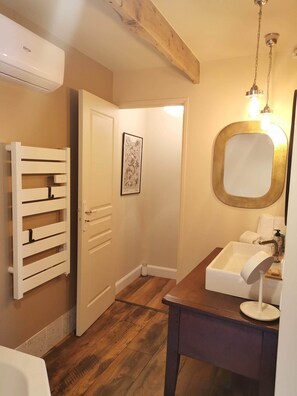 A bathroom with a wooden floor, a white sink with a mirror, a towel rack, and an air conditioning unit.