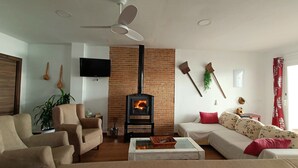 Un salon avec une cheminée en briques, un ventilateur de plafond et un téléviseur fixé au mur.