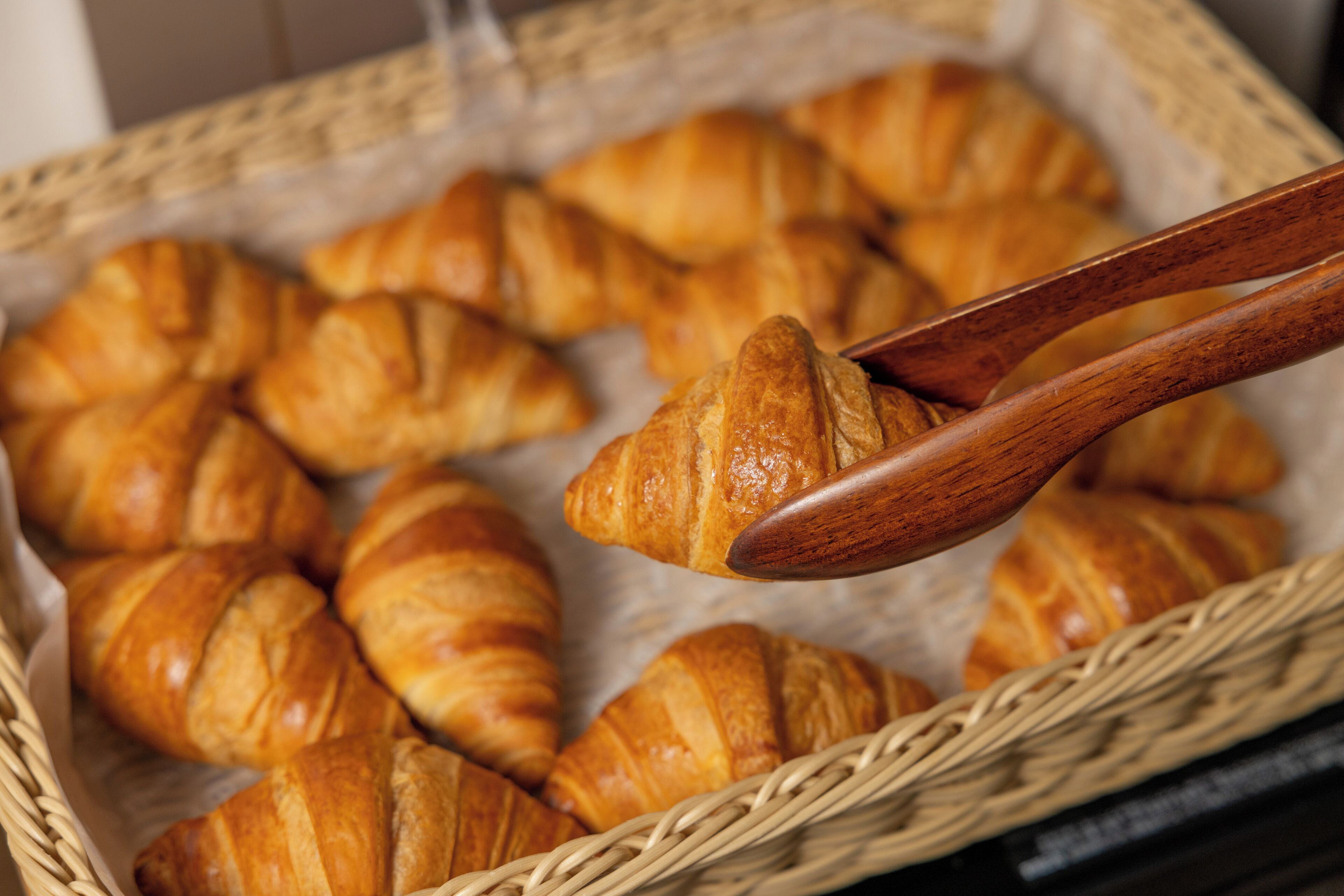 En kurv med croissanter, hvor en træske løfter en af dem.