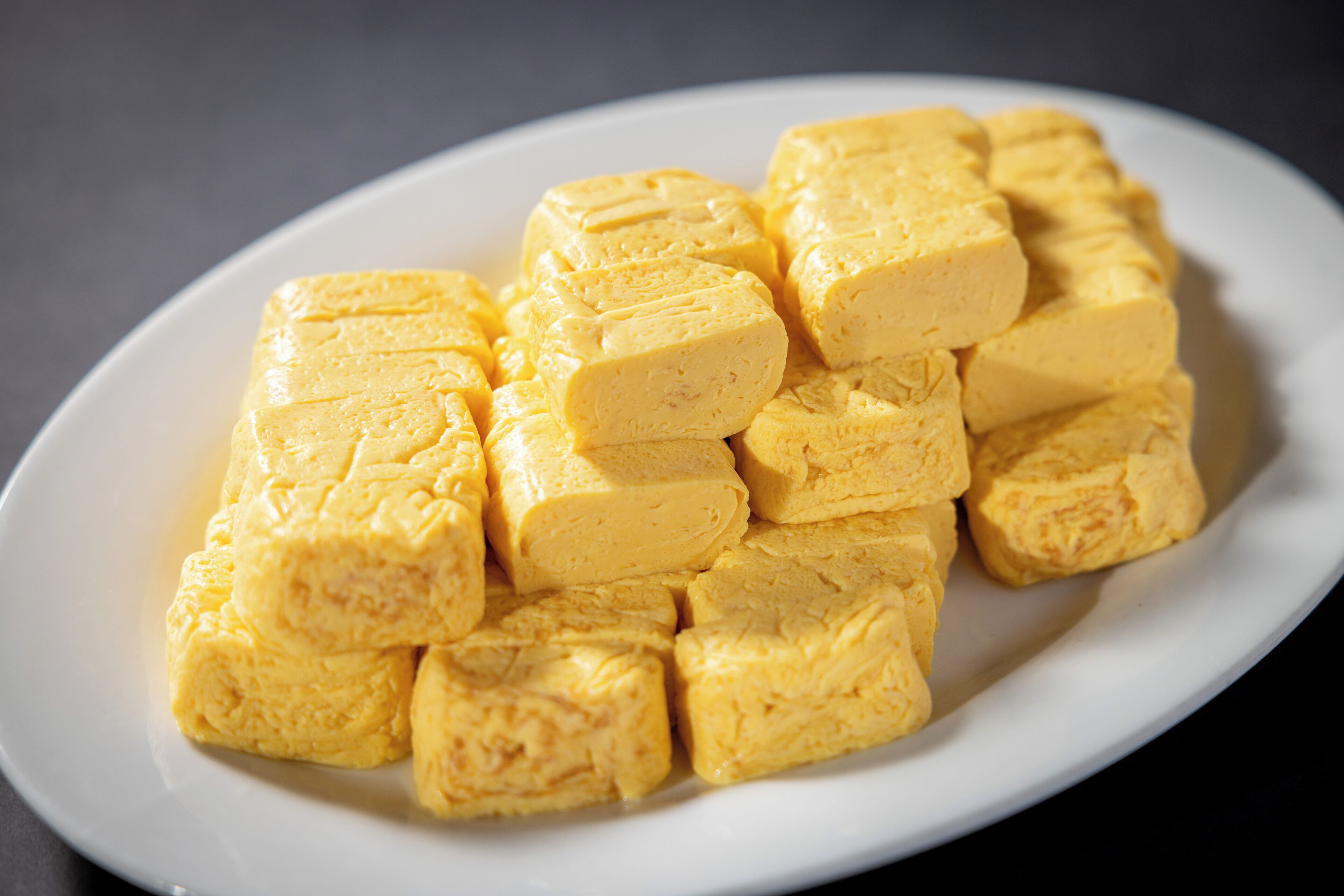 A white oval plate filled with neatly cut, yellowish blocks of tofu.