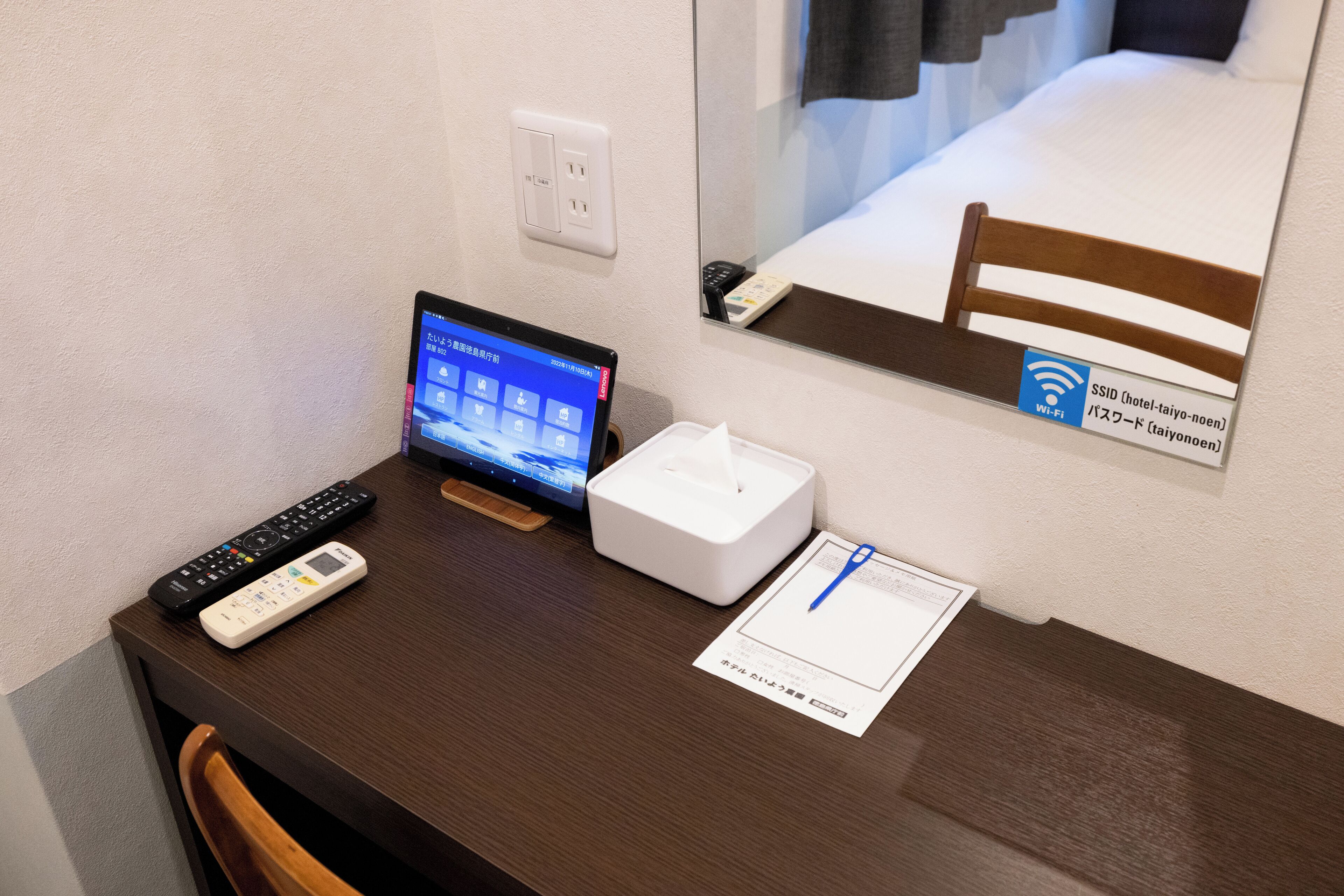 A hotel room desk with a laptop, a remote control, a tissue box, and a Wi-Fi sign.