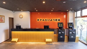 Zona de recepción de un hotel con un mostrador de madera, un reloj y un amplio ventanal.