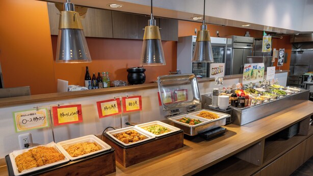 Zona de bufé con varias estaciones de comida, incluyendo bandejas con alimentos fritos y ensaladas, bajo iluminación colgante.