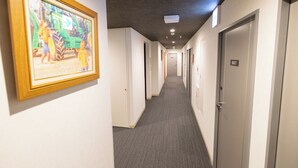 Un pasillo de hotel con piso alfombrado, paredes blancas y puertas a la derecha.