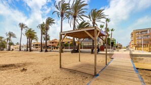Eine am Strand stehende Holzkonstruktion mit Dach, umgeben von Palmen und einem Sandstrand.