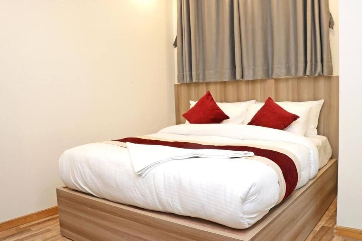 A neatly made bed with white bedding and red pillows, a wooden headboard, and a light-colored wall.