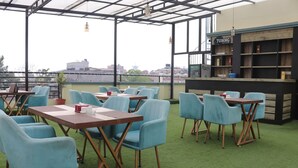 An outdoor seating area with tables and chairs, a bar, and a view of the cityscape. - Hotel Royal Emperor (Kathmandu)