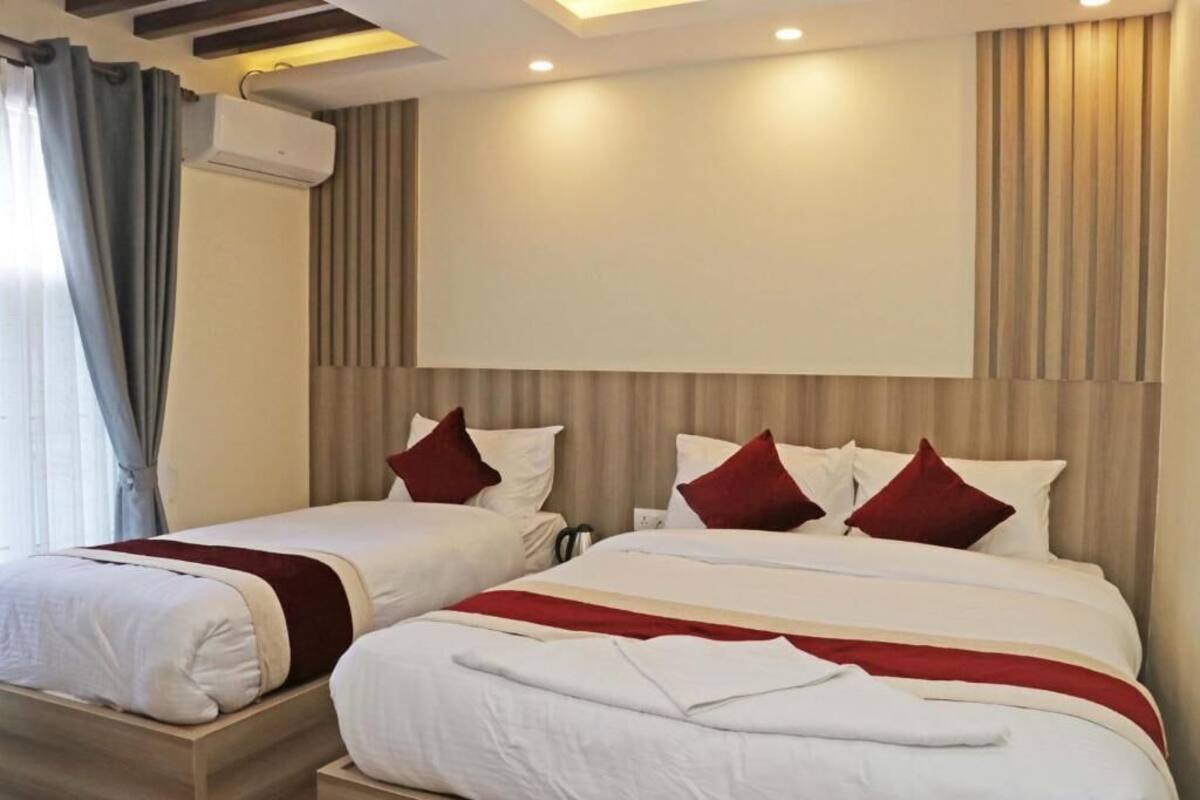 A hotel room with two beds, a large window with curtains, an air conditioning unit, and a neutral color scheme.