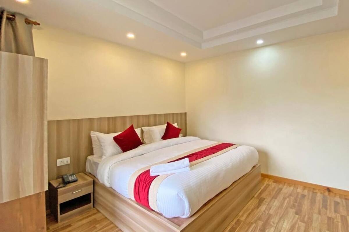 A hotel room with a wooden bed, white bedding, and red pillows.