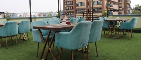 A rooftop terrace with green artificial grass, teal chairs, and wooden tables.