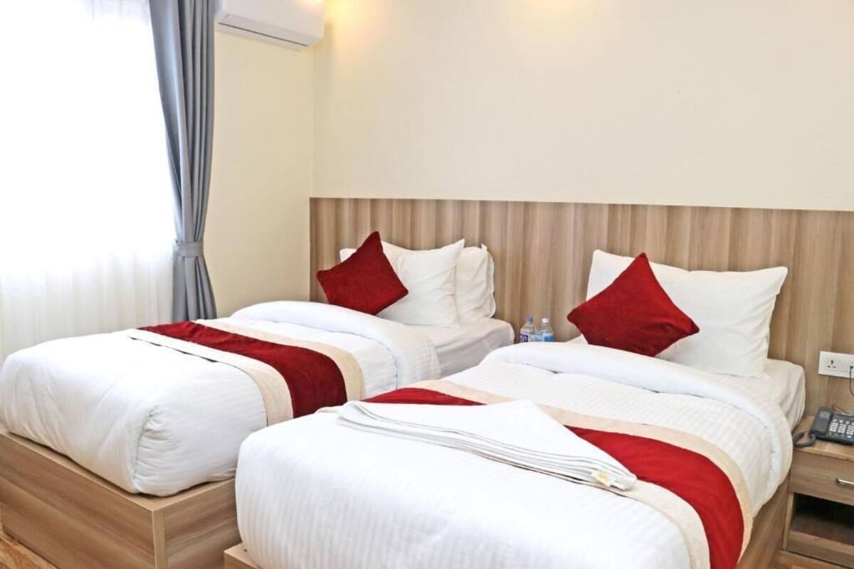A hotel room with two beds, each with white bedding and red accents, a wooden headboard, and a bedside table with a phone.