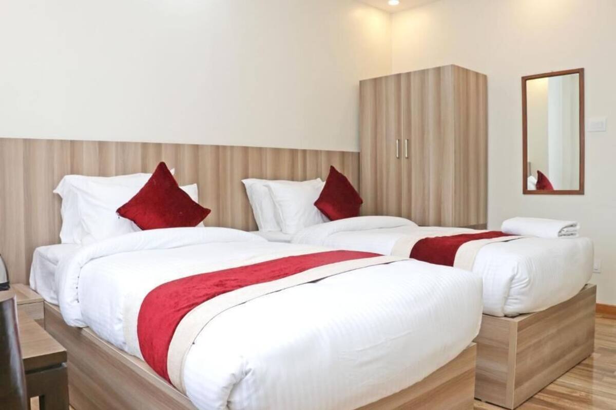 A hotel room with two beds, each with white bedding and red accents, a wooden wardrobe, and a mirror on the wall.