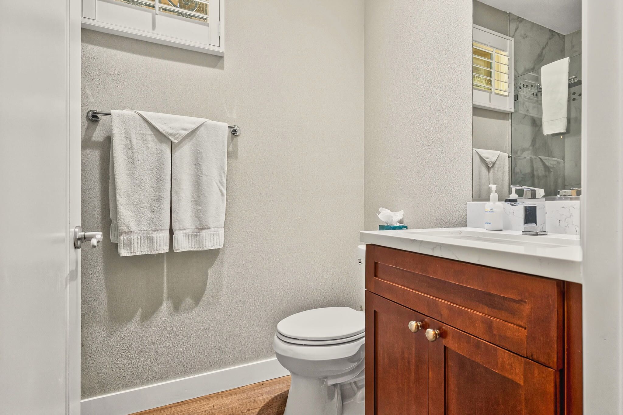 Een badkamer met een wit toilet, een houten wastafelmeubel en een handdoekrek met twee handdoeken.