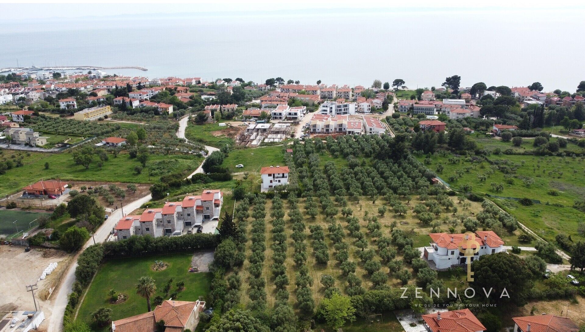 Vista aérea de una zona residencial con casas, olivares y un puerto deportivo.