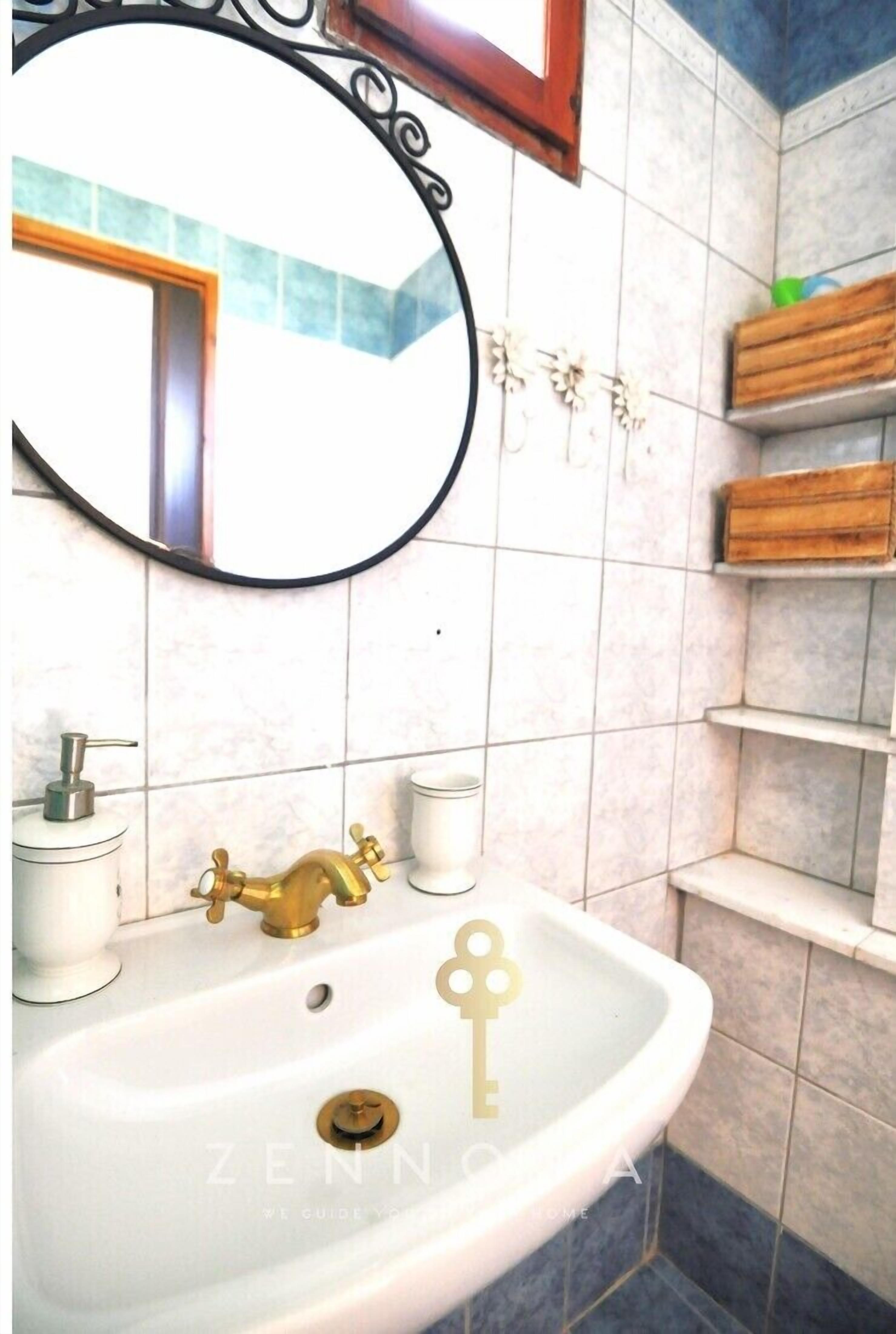 Un baño con lavamanos blanco, grifo dorado y espejo con marco negro.
